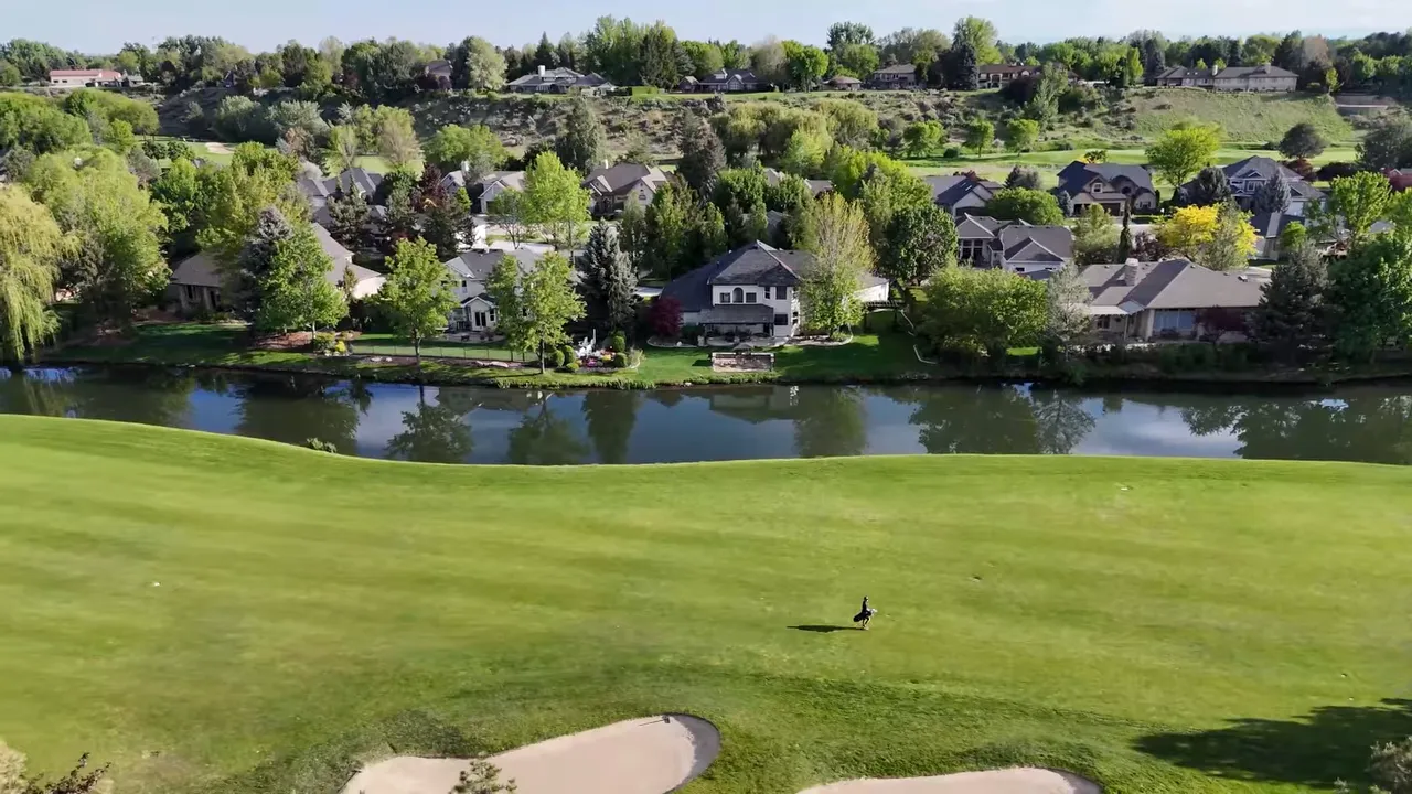 Golf course fairway beside a pond with homes in the background