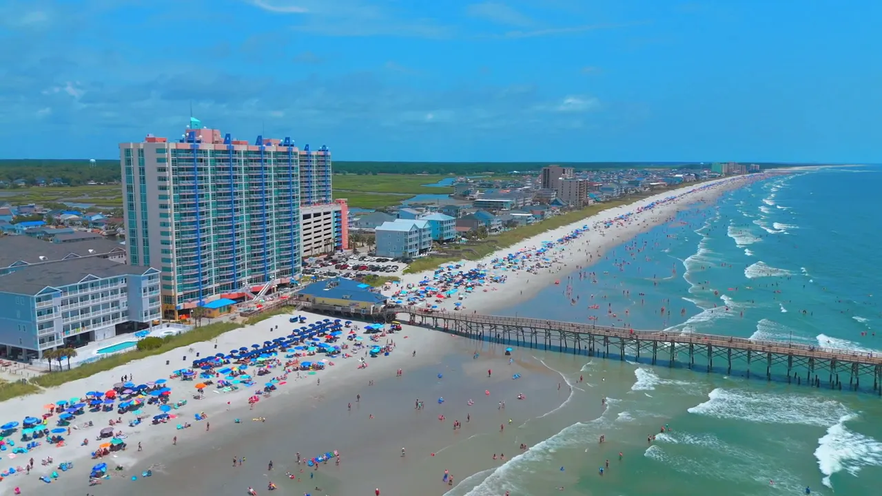 Aerial view of Myrtle Beach showing packed beach umbrellas, swimmers and a long pier.