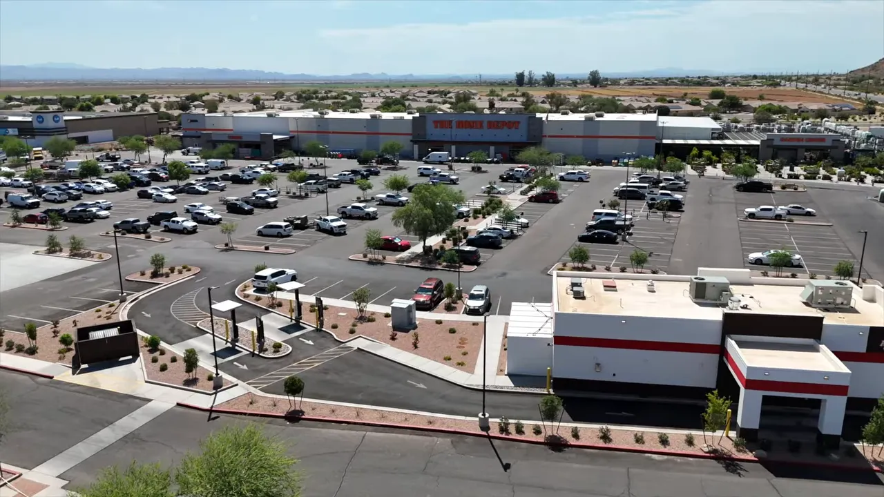 Aerial view of a large parking lot, commercial buildings, and surrounding development