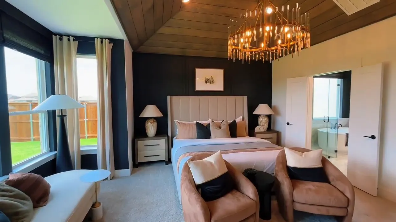 Primary bedroom with large bed, two accent chairs, chandelier, and dark feature wall