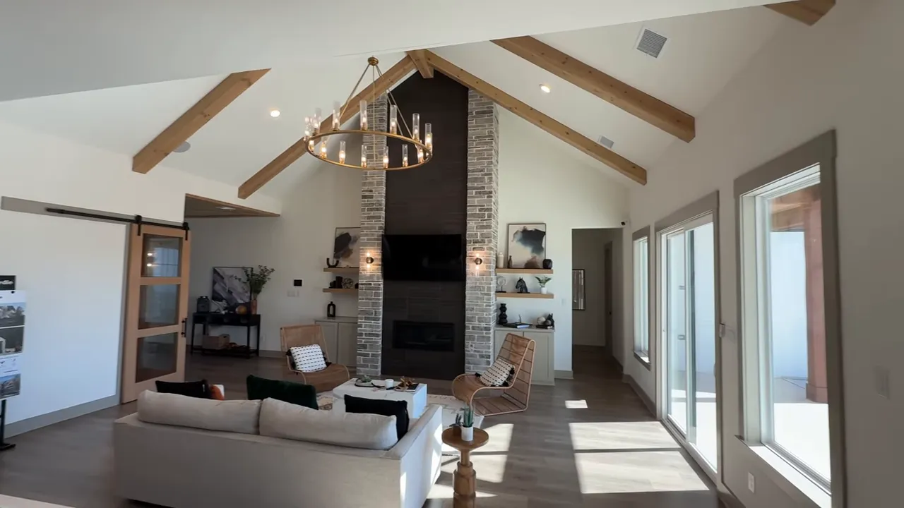 Vaulted living room with exposed wooden beams, brick fireplace, chandelier and sliding glass doors