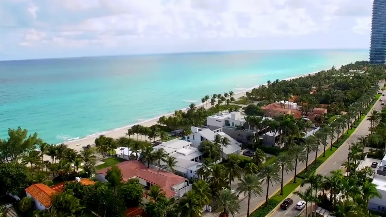 Aerial view of luxury beachfront homes with palm trees and private shoreline in South Florida
