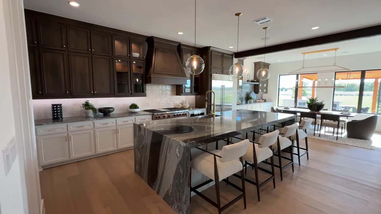 Spacious kitchen with large waterfall island, pendant lights, dining nook and living room beyond