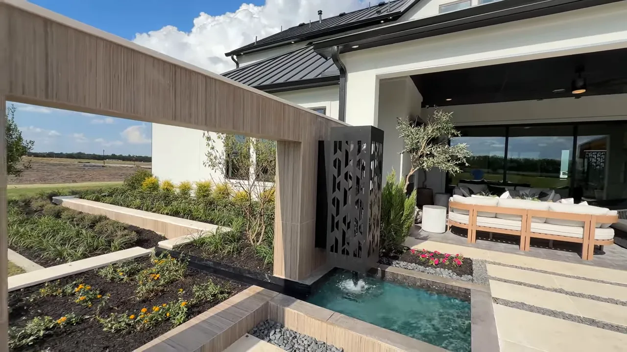Covered patio with waterfall fountain, landscaped beds and outdoor seating at Toll Brothers model
