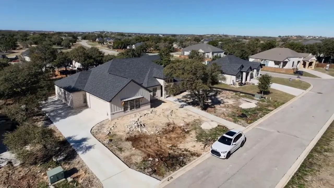 Drone view of a Rancho Del Lago spec home with a large oak tree, driveway and adjacent lots under development