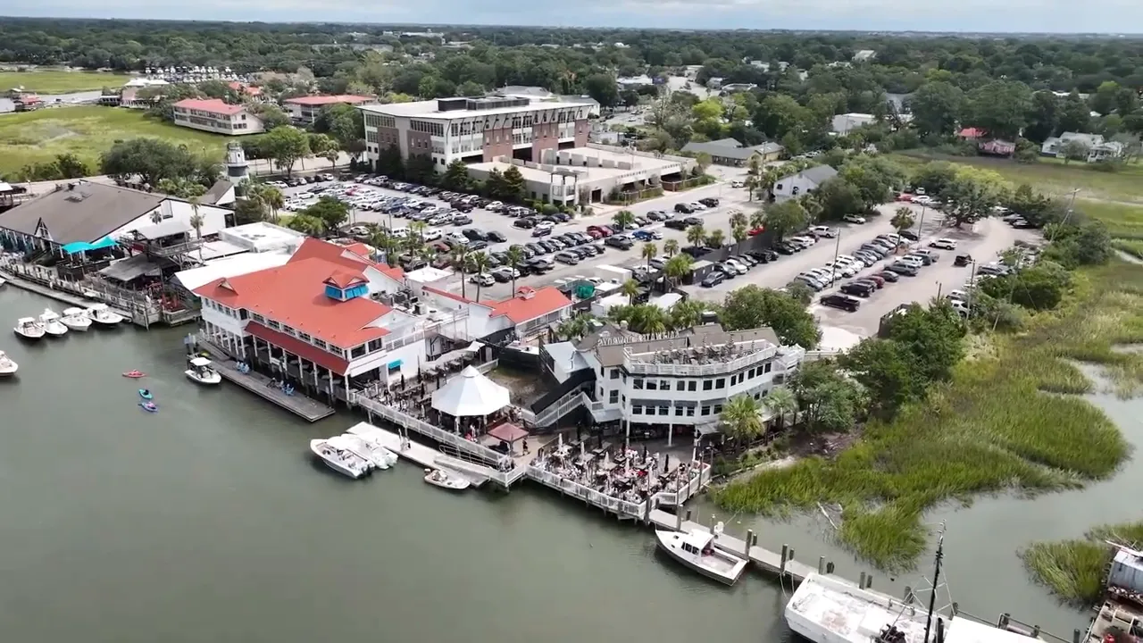 Aerial view of a waterfront marina area with buildings and parking lot in Charleston area