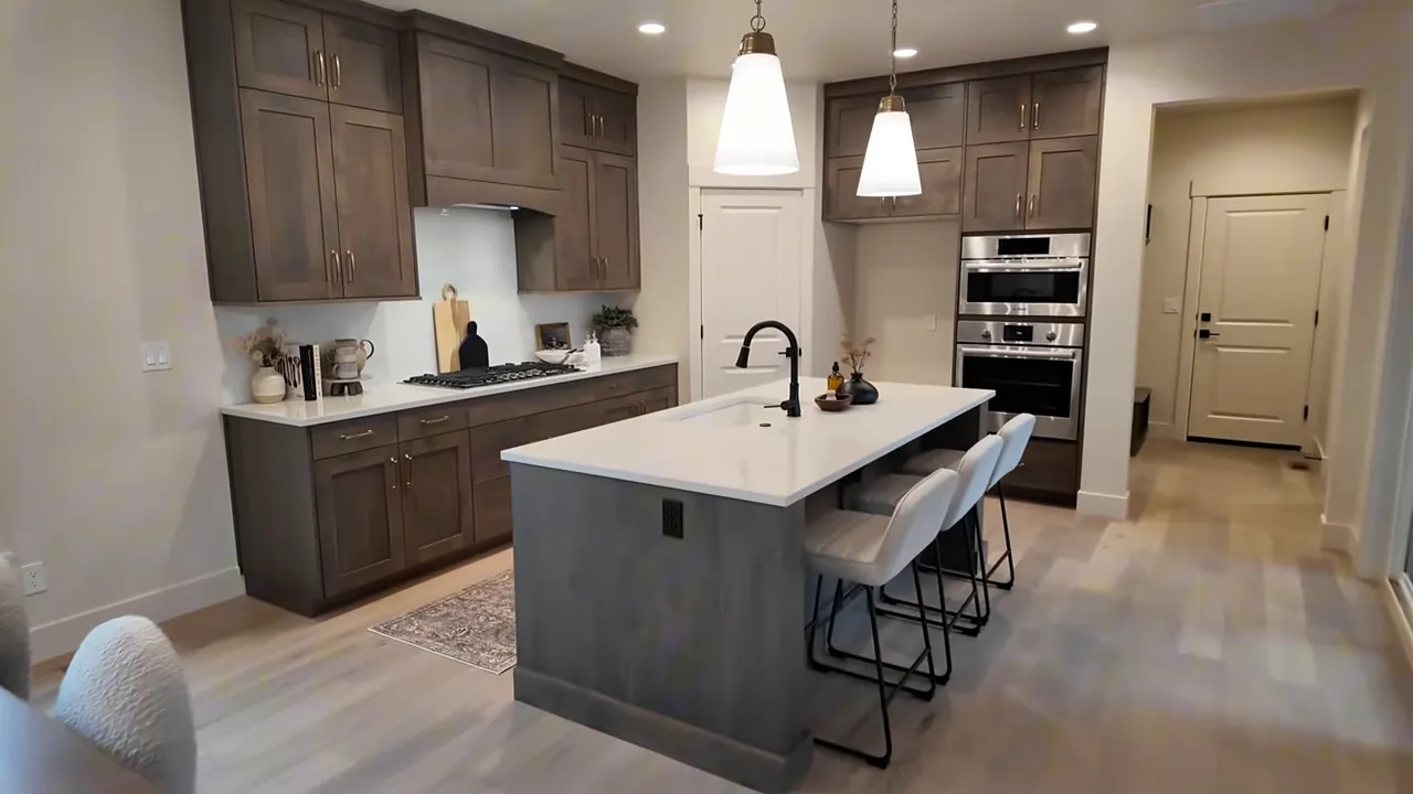 Kitchen island with white countertop and seating, pendant lights, tall wood cabinets, statement hood and stacked wall ovens