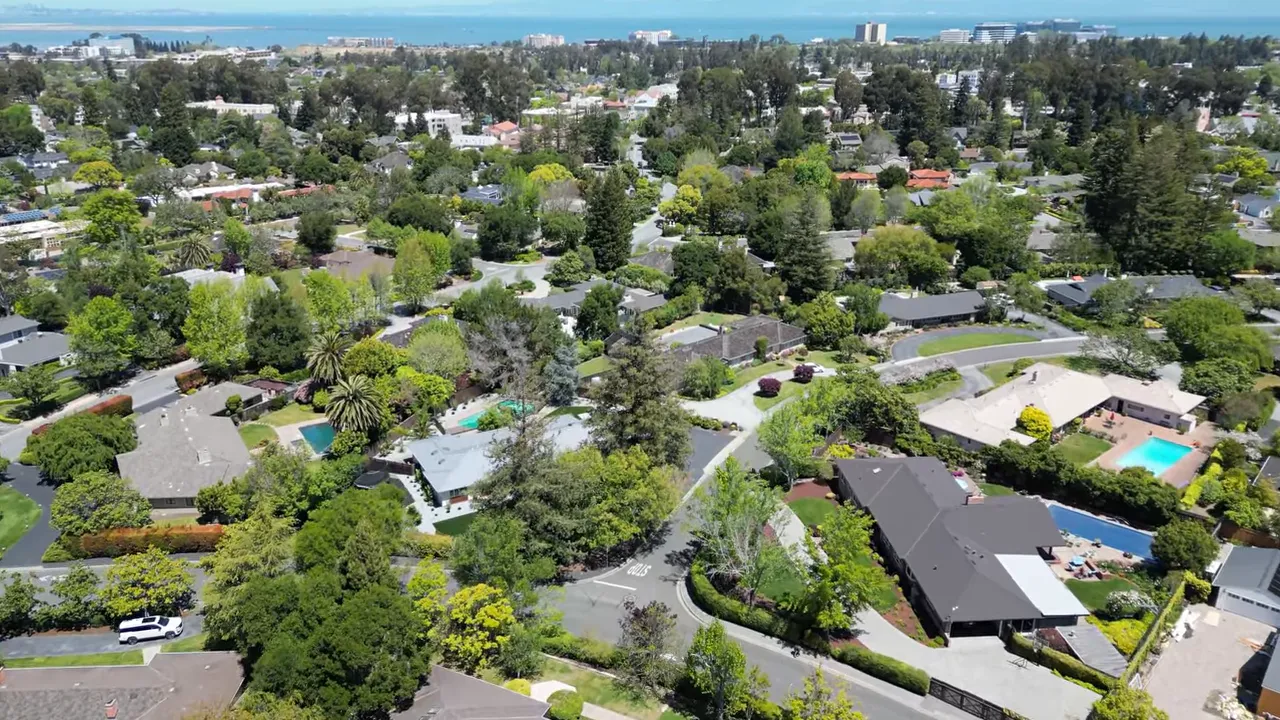 Wide aerial view of San Mateo County neighborhoods showing rooftops, trees, and coastal horizon