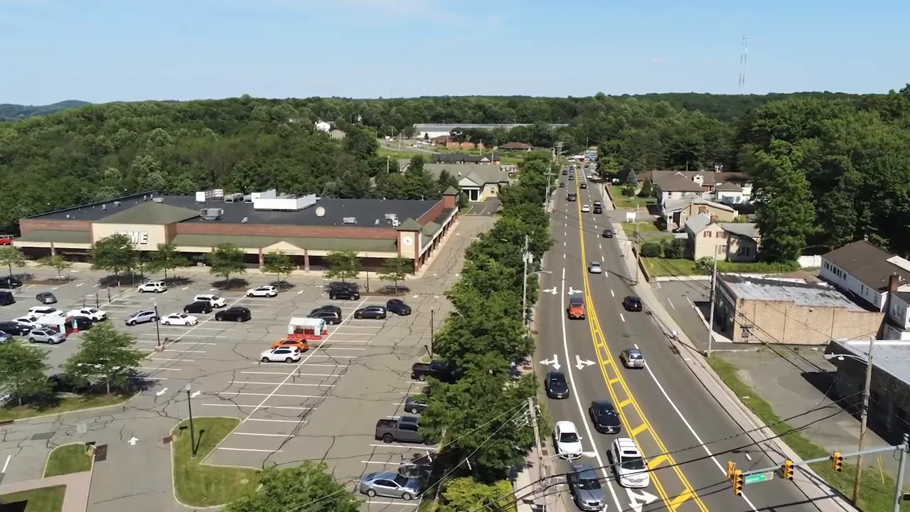 Aerial view of a commercial road with parking lots shops and passing traffic