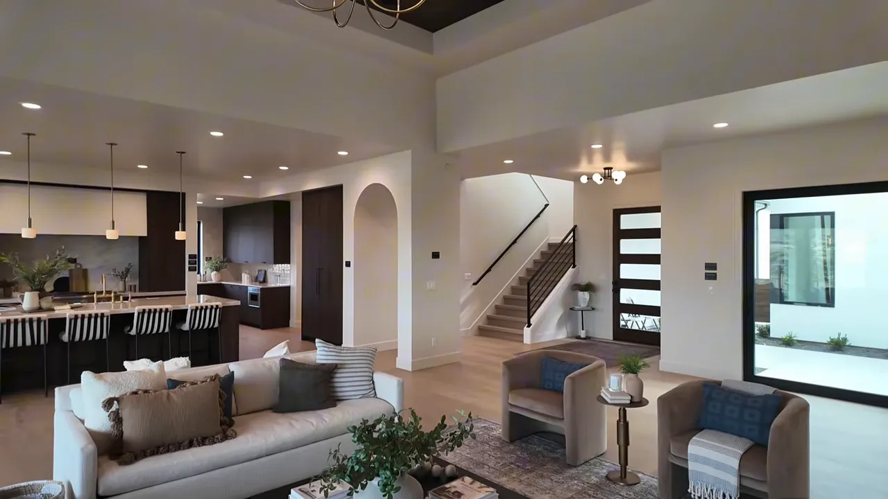 Wide open-plan view of kitchen and living area showing island, quartzite counters, stained walnut cabinets, arches and staircase