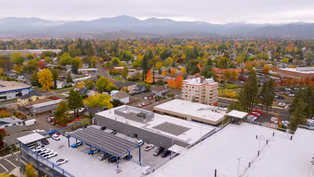 Panoramic aerial of Southern Oregon neighborhoods stretching toward distant mountains, showing housing spread and landscape.