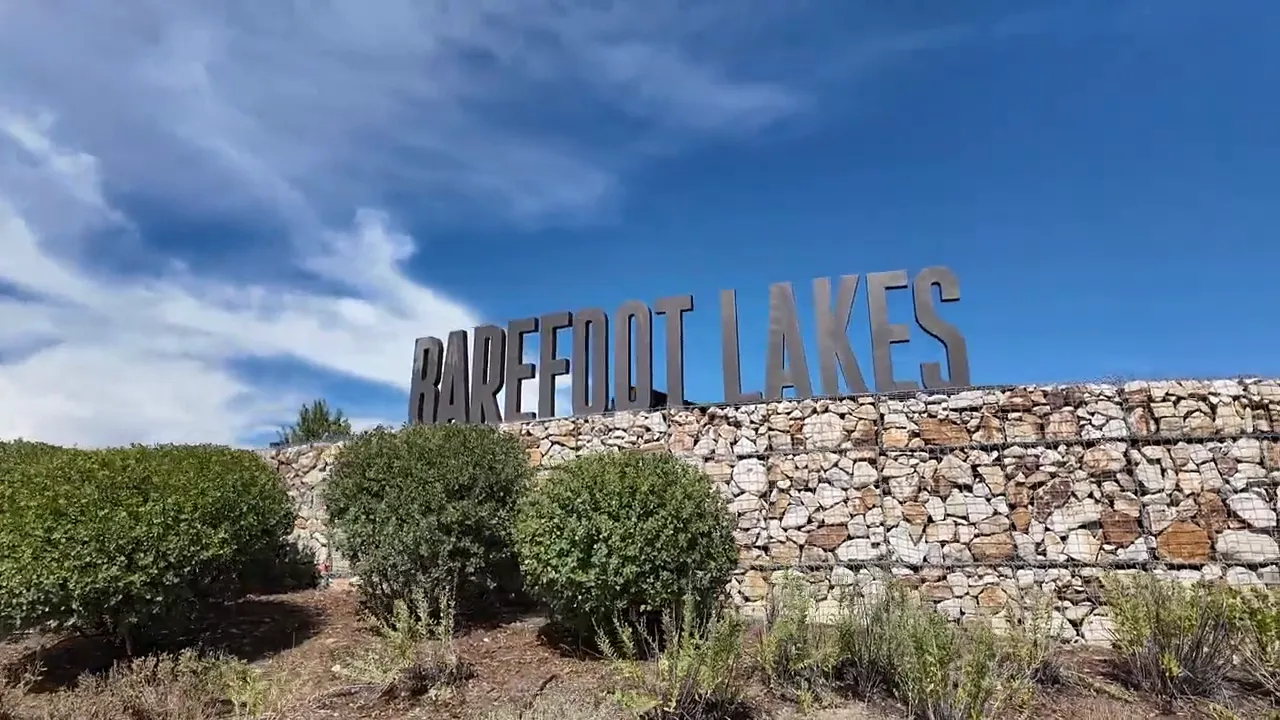 stone entry wall with Barefoot Lakes sign above landscaped shrubs