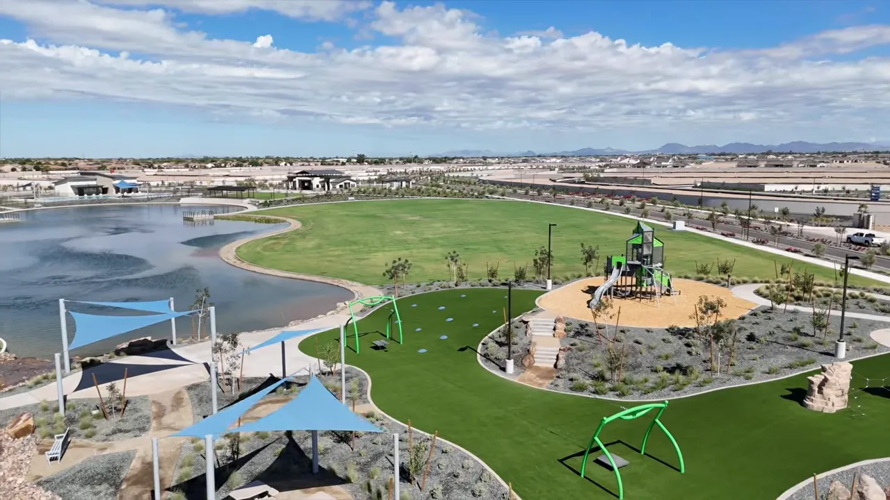 Aerial view of large park with playground area, lawn, and lakeside path at Soleado