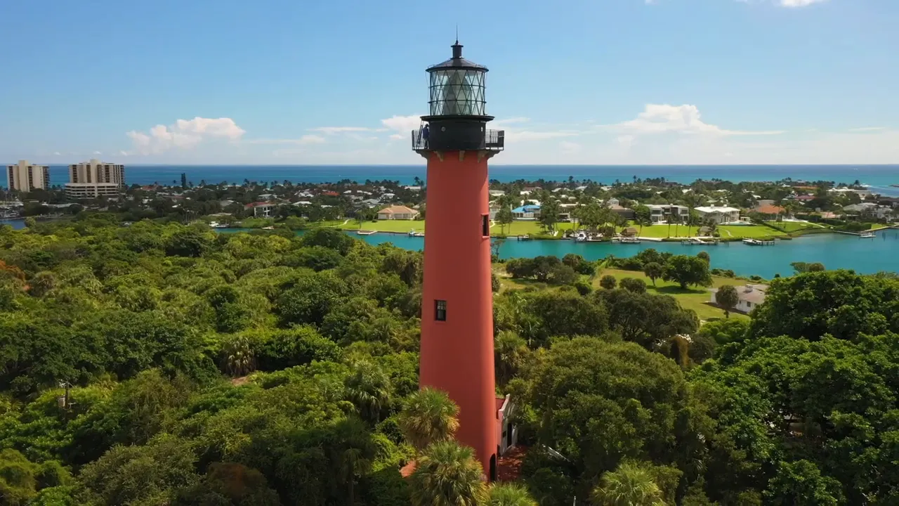 Red Jupiter Inlet Lighthouse rising above green trees with blue water in the background
