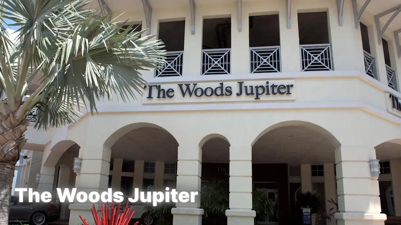 Entrance to The Woods Jupiter restaurant with arched facade and palm trees
