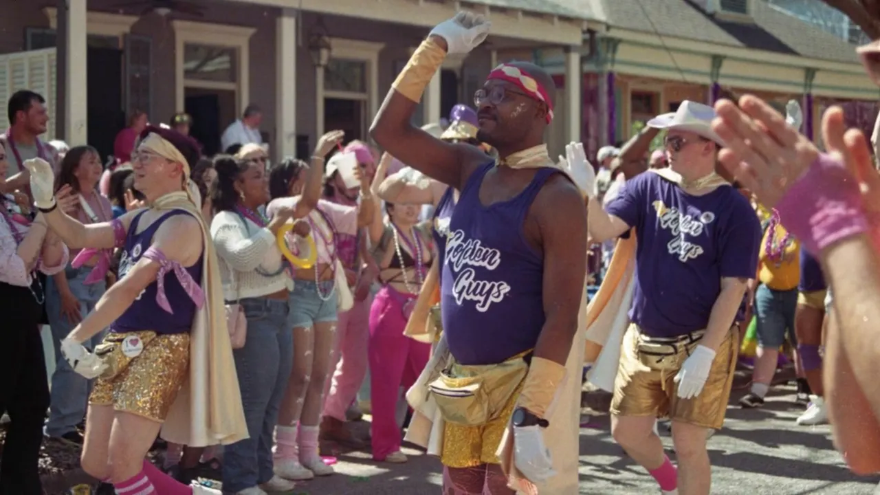 Crowded street parade with people in purple and gold 'Golden Guys' costumes and cheering spectators