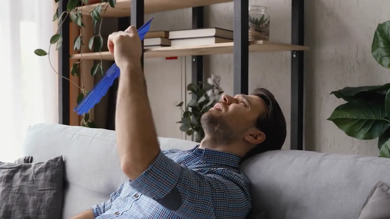 Person fanning themselves on a couch demonstrating oppressive indoor heat