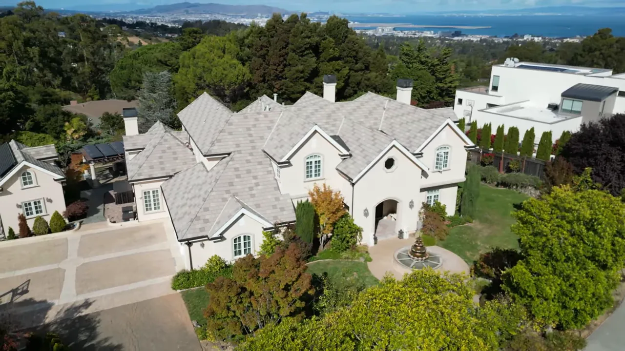 Aerial shot of a large hilltop estate with multiple rooflines and distant bay/Oakland hills in the background.