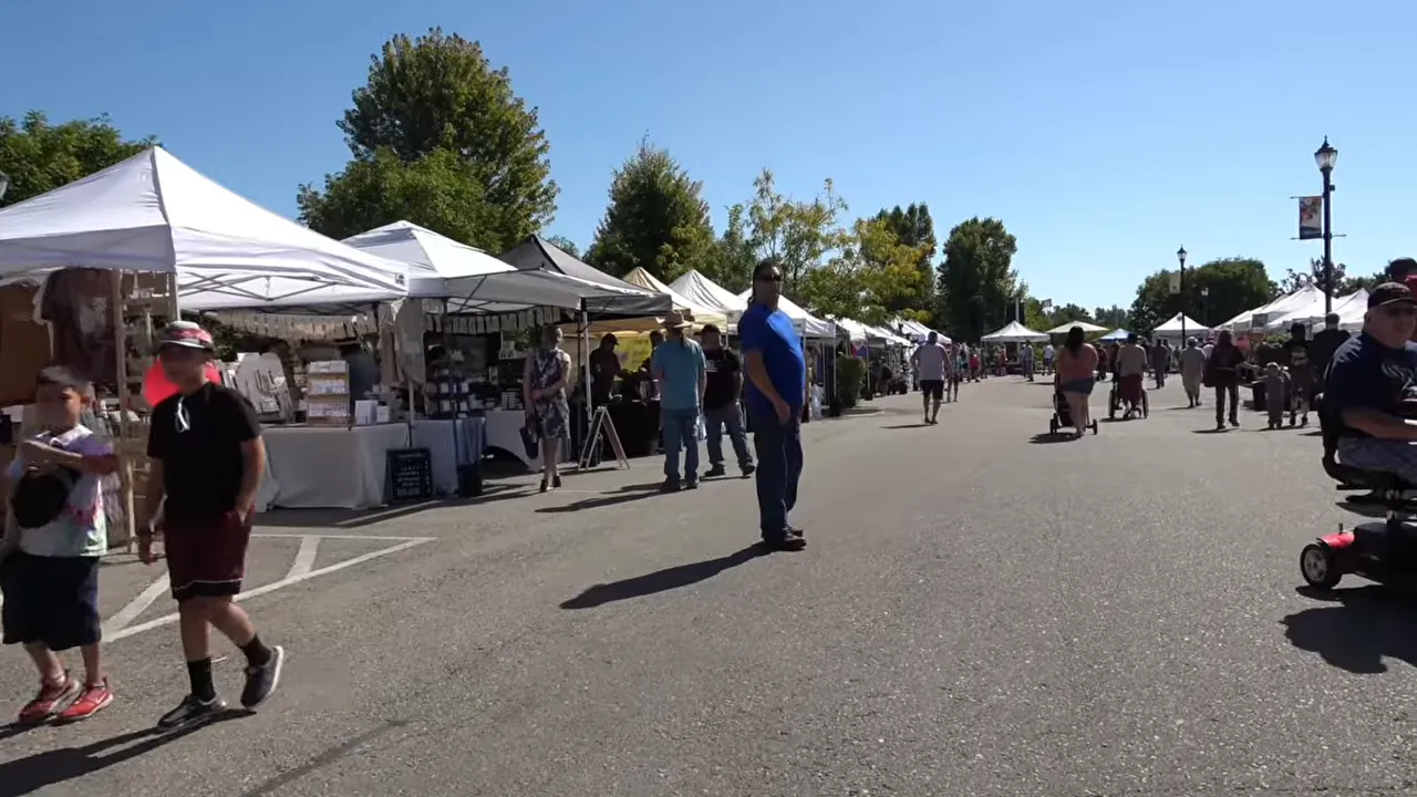Outdoor market with white vendor tents and people walking between booths