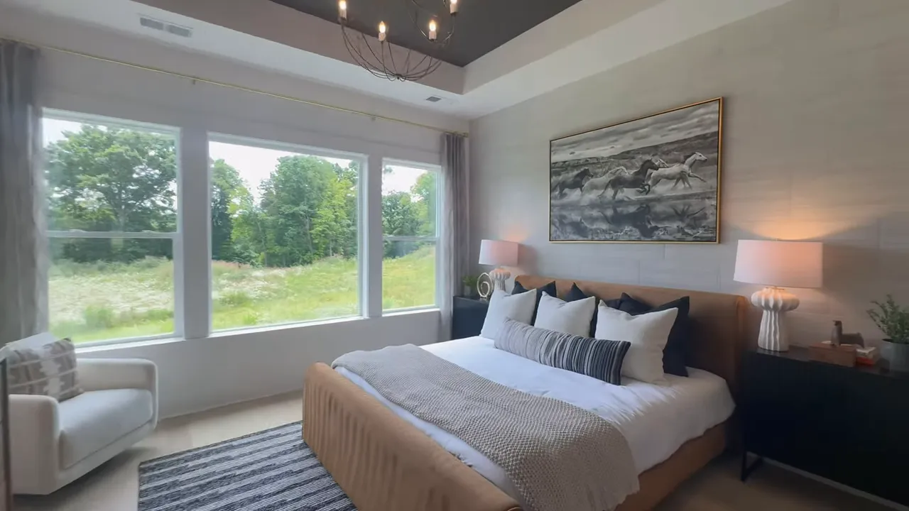 Primary bedroom with tray ceiling large windows and bed facing meadow view