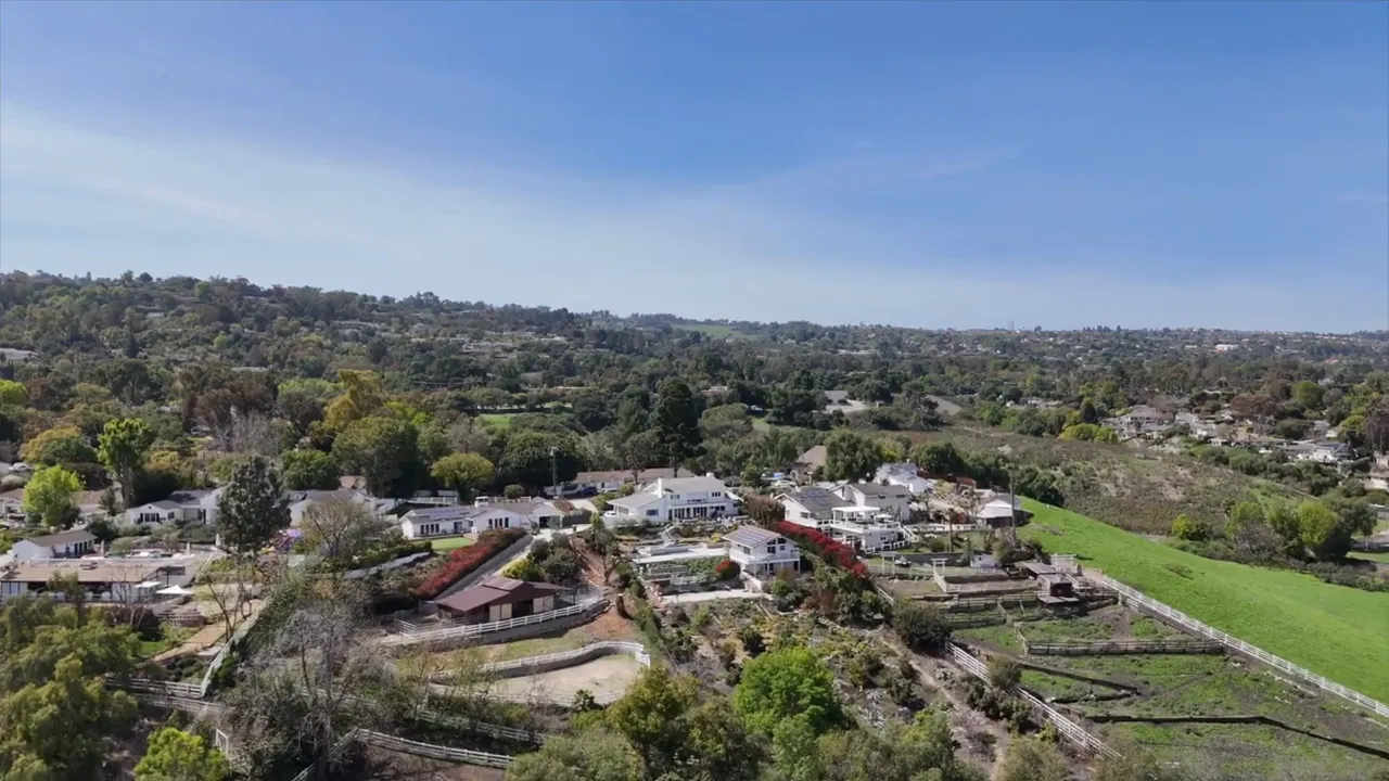 Aerial view of homes with fenced paddocks, riding areas, and terraced lots beside green open land