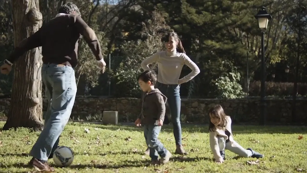 Family playing soccer together in a sunny park