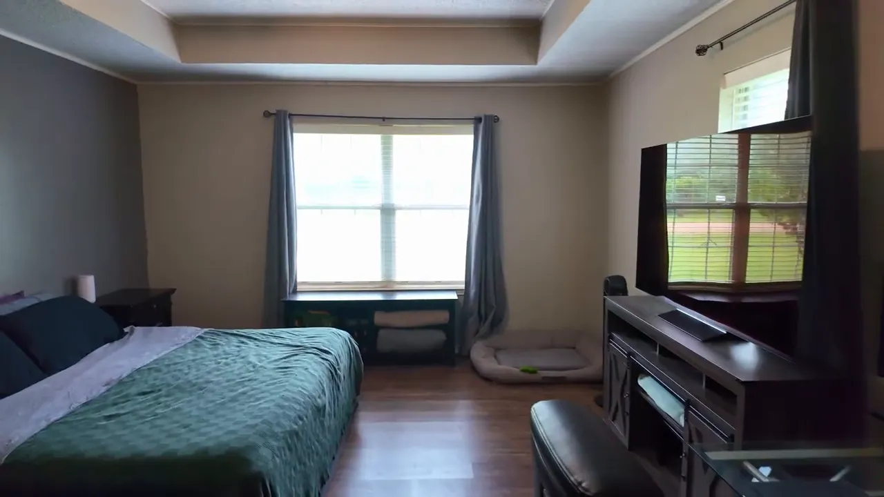 Primary bedroom with tray ceiling large television desk and window