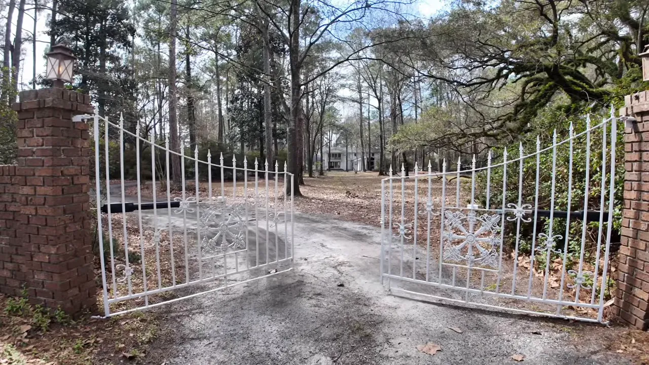 View through a white metal gate at a brick entrance down a private driveway in Summerville SC