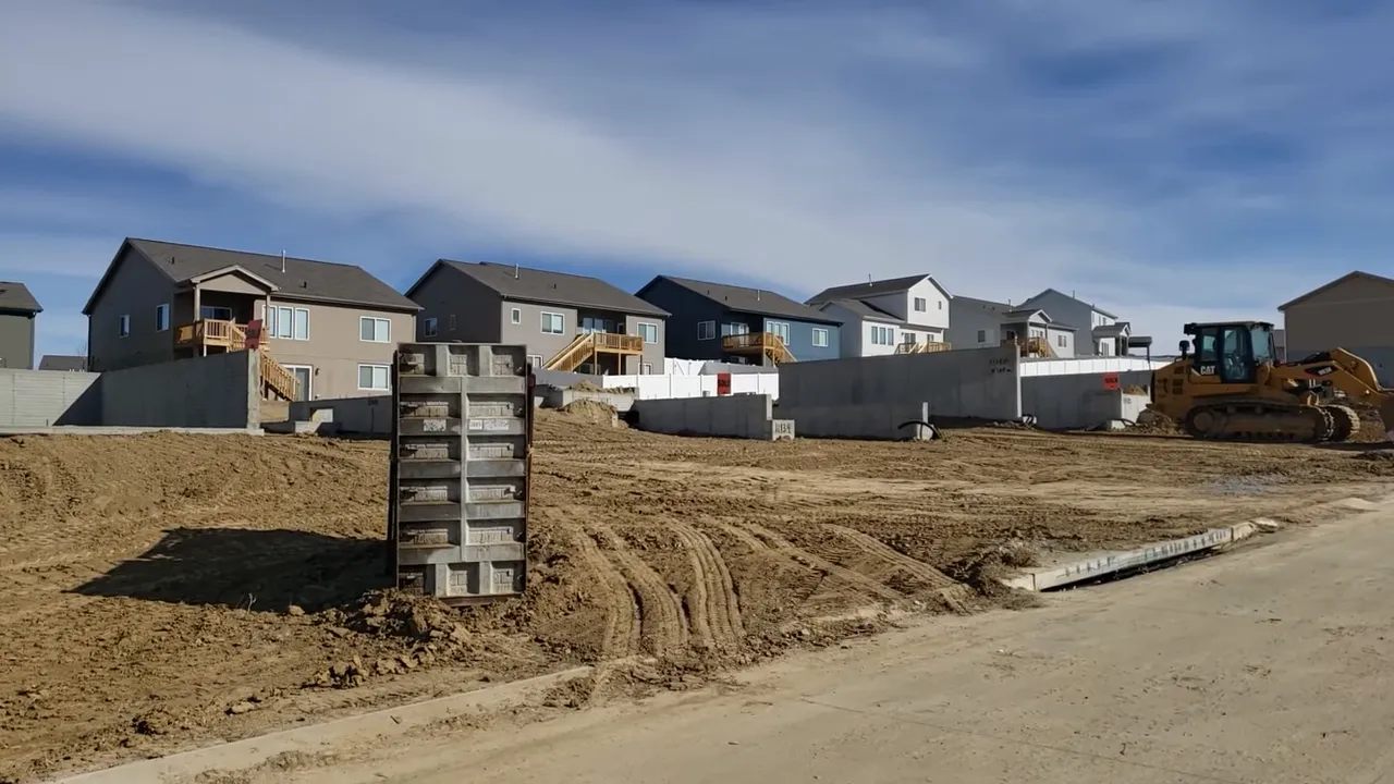 Suburban new-home construction lot with concrete foundations, tire tracks in dirt and a bulldozer at the edge.