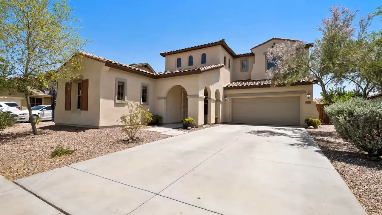 tan stucco house with driveway and two car garage under blue sky