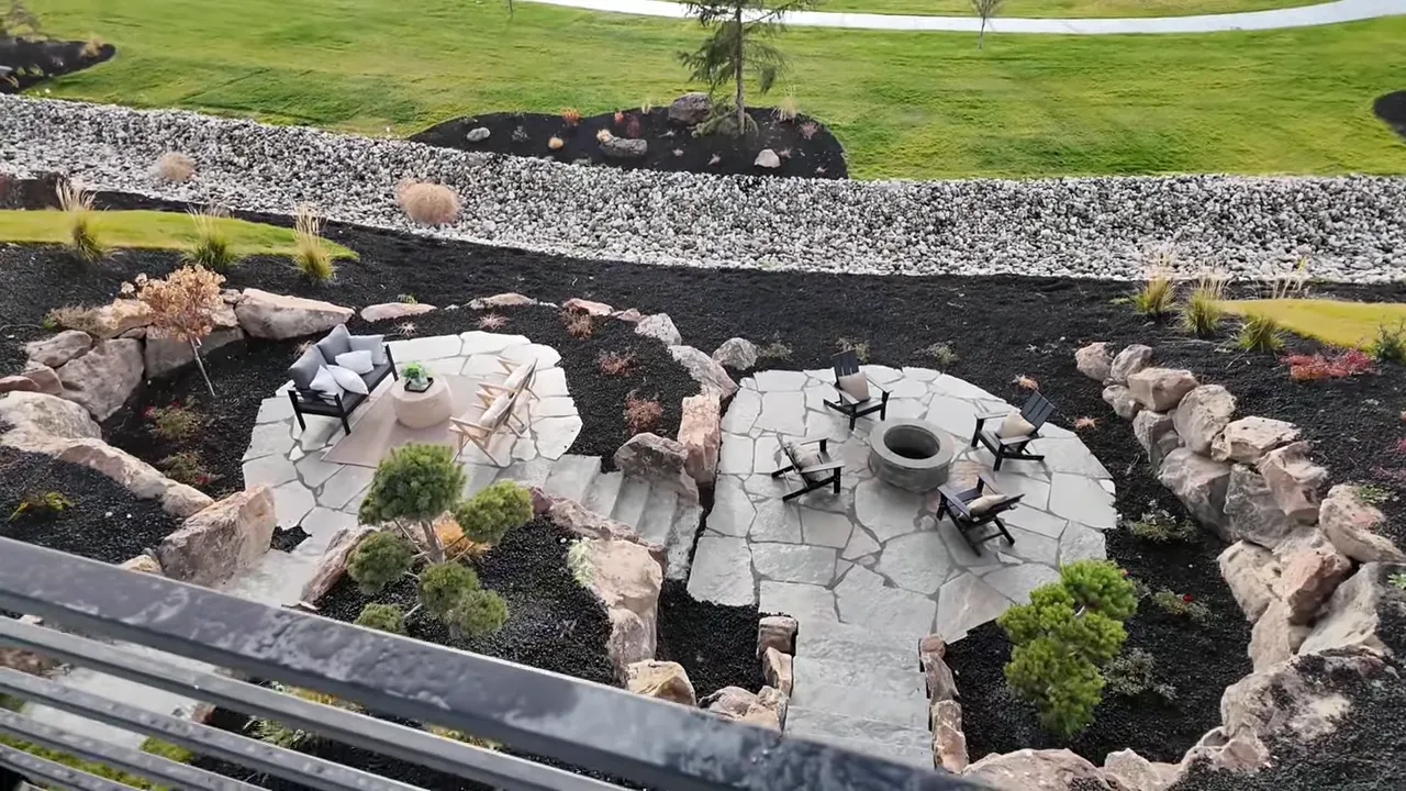 Terraced lower patios with seating and a central firepit, rock landscaping and the park lawn beyond.