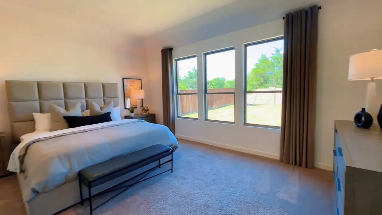 Primary bedroom with large bed bench and three tall windows facing the backyard