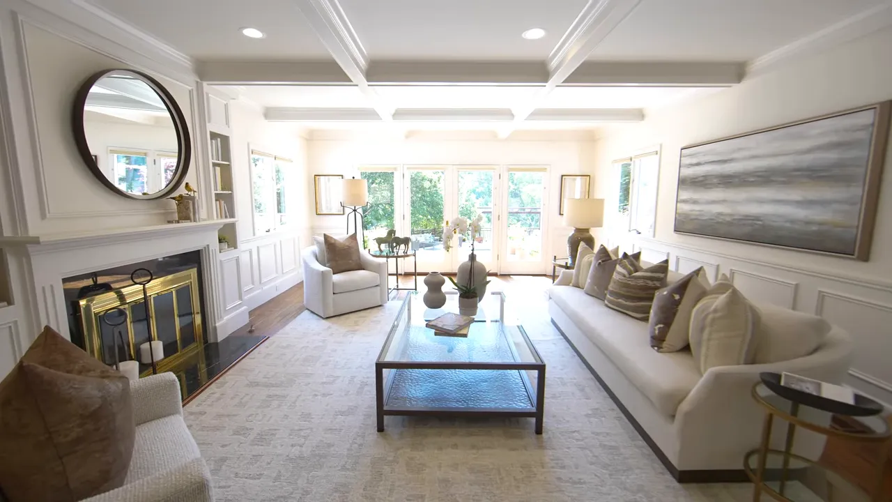 Bright staged living room with coffered ceiling, fireplace, seating and glass doors opening to the backyard