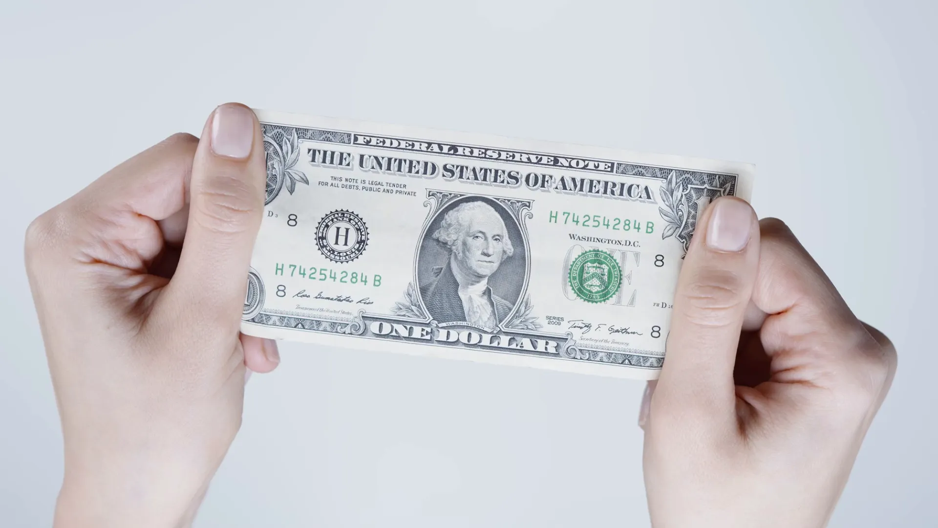 Close-up of hands holding a one dollar bill against a light background, symbolizing money and buyer costs.