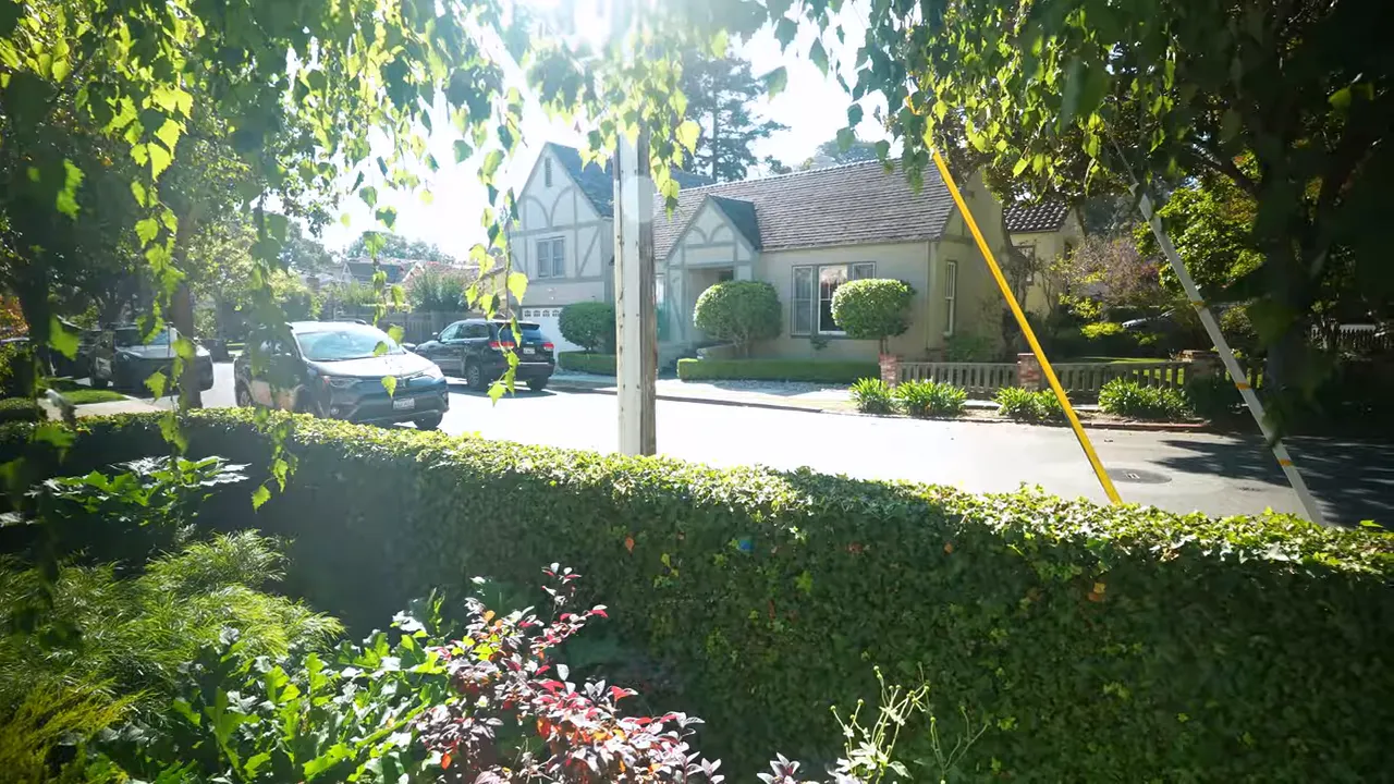 Sunlit streetscape with Tudor-style house, trimmed hedges, mature street trees and parked cars in Easton Addition, Burlingame