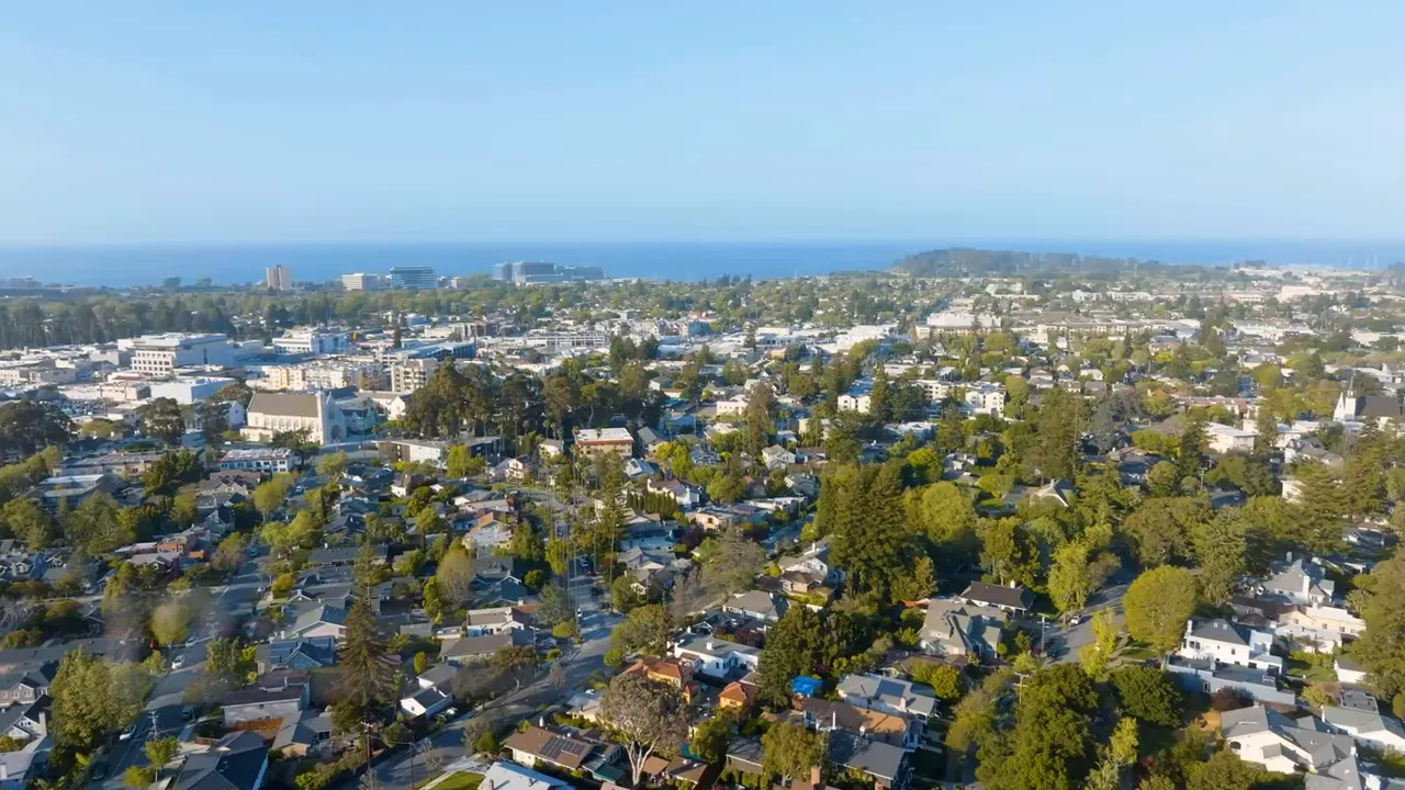 Aerial view of Burlingame neighborhood with houses, mature trees, and the bay on the horizon