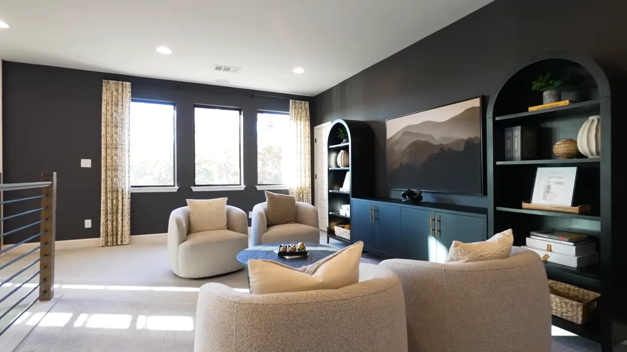 Bright upstairs game room/media lounge with rounded chairs, coffee table, built-in media cabinet and three windows providing natural light.