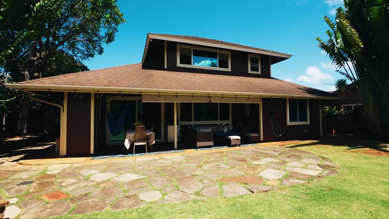Wide view of a Mililani home's backyard, stone patio and covered outdoor seating under a blue sky
