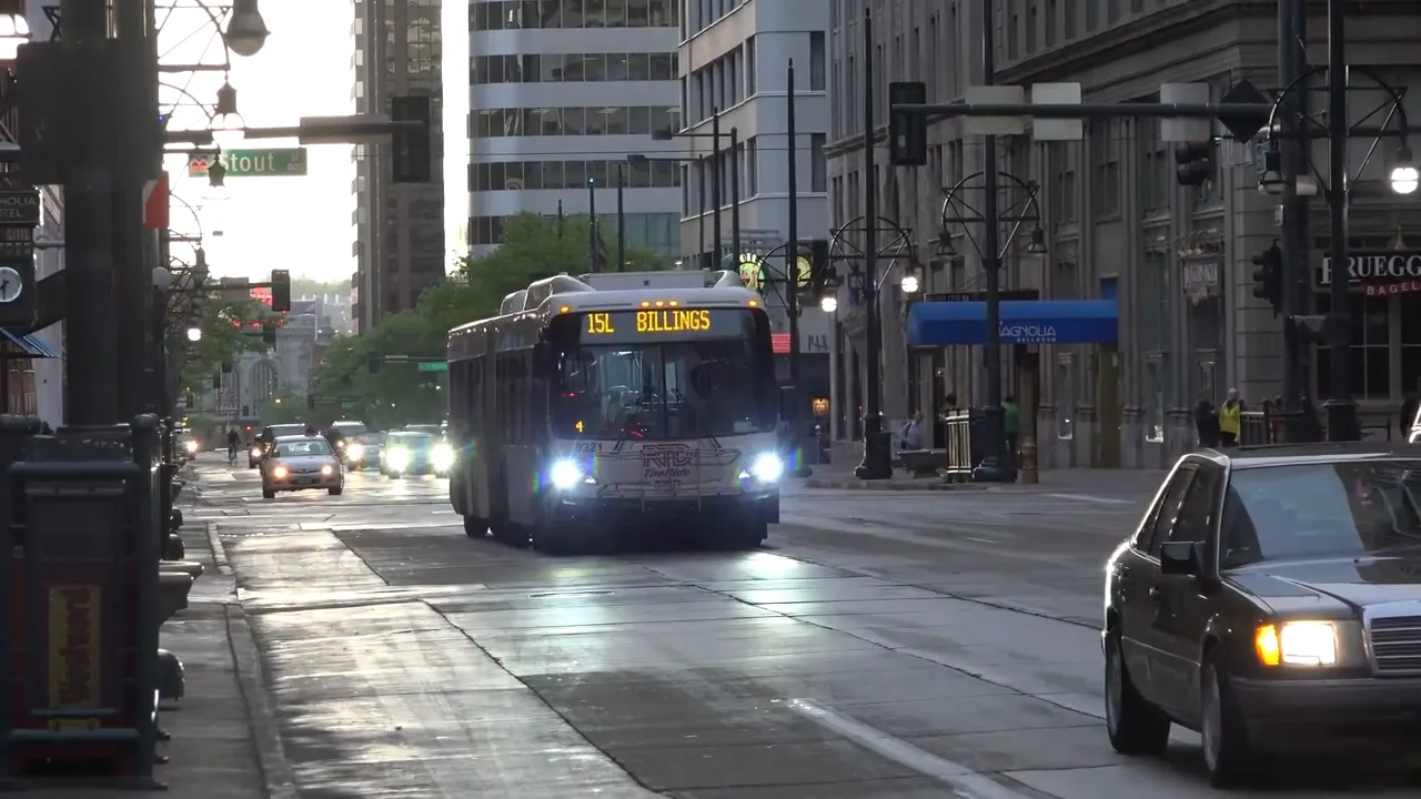 Large city bus approaching on a downtown roadway with cars and street infrastructure