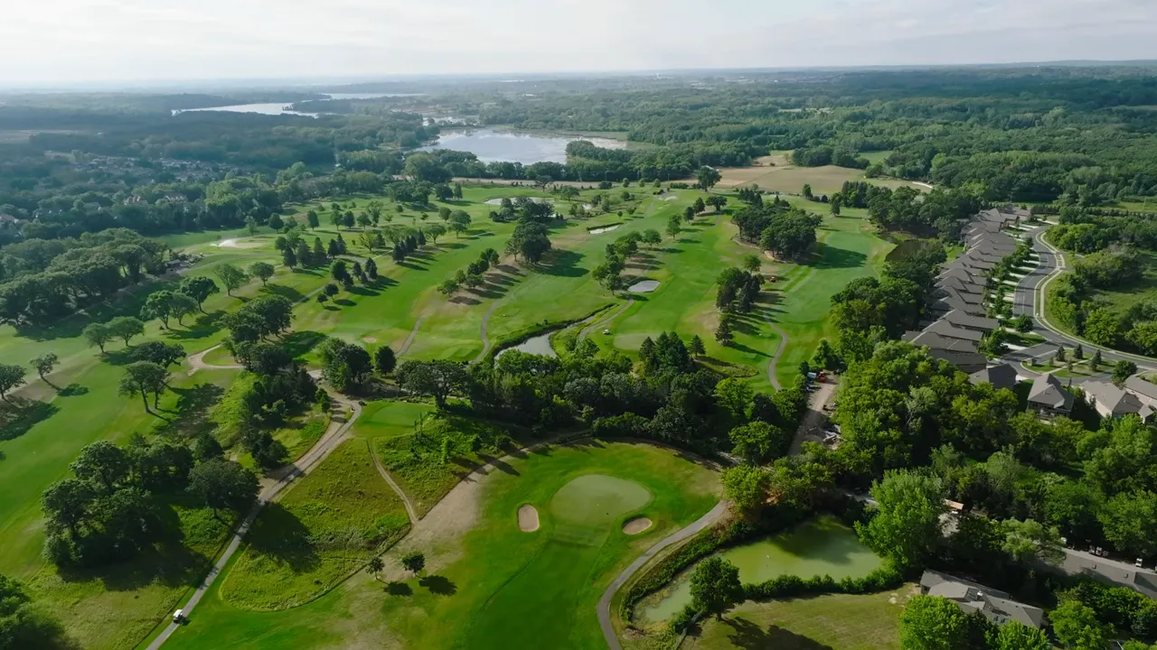 Aerial view of a golf course with fairways, greens, water hazards and nearby residential community