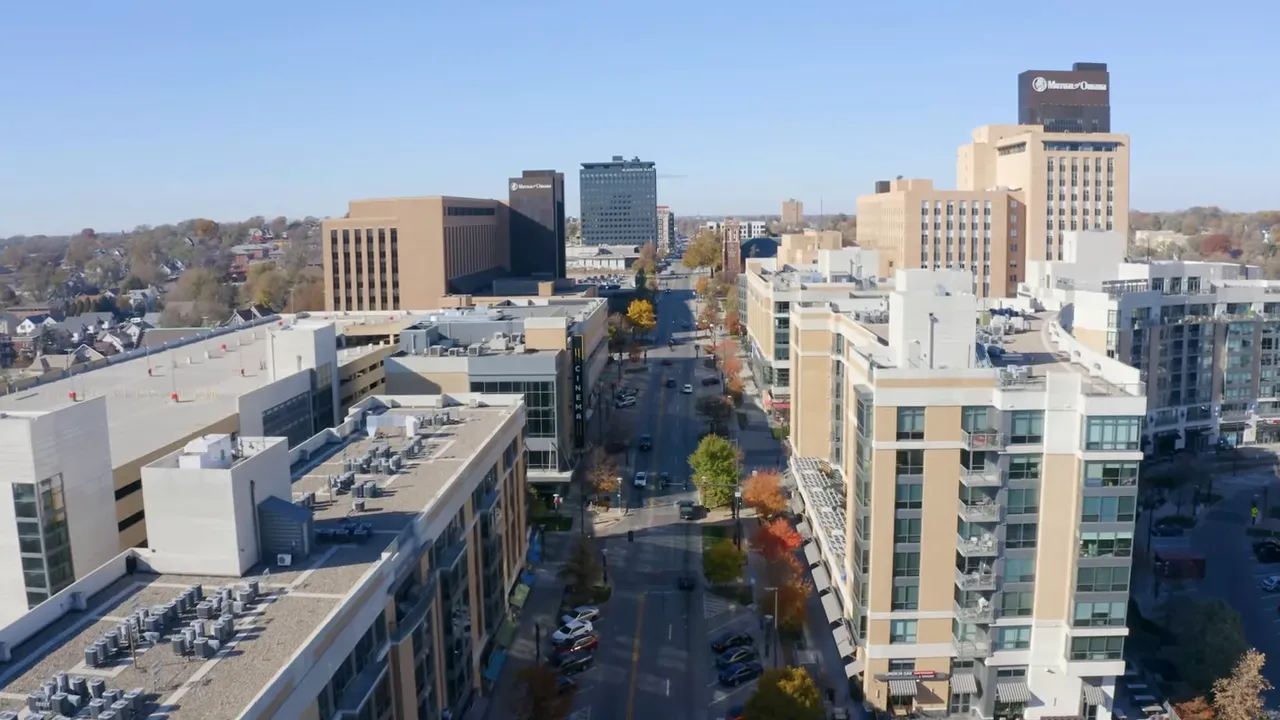 Aerial view of a downtown street in Omaha with mid-rise buildings, light traffic and clear skies.