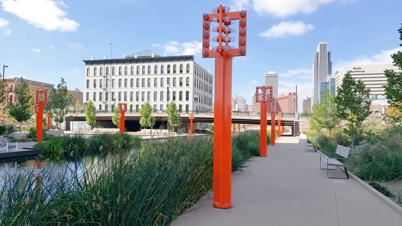 Omaha riverfront park walkway with orange light poles, benches, and downtown skyline in the background
