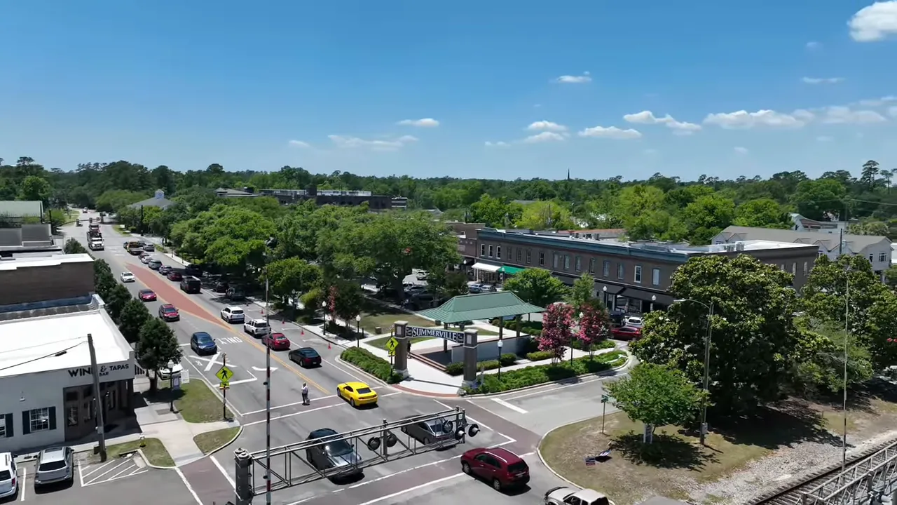 Clear aerial photo of Summerville pavilion and main street showing cars, crosswalks, trees, and nearby businesses.