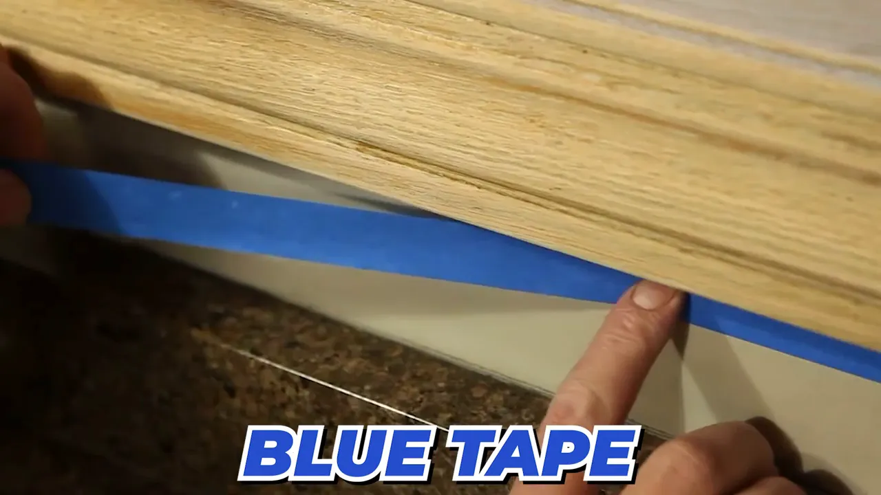 Close up of blue tape being placed along a wood trim edge with text reading blue tape