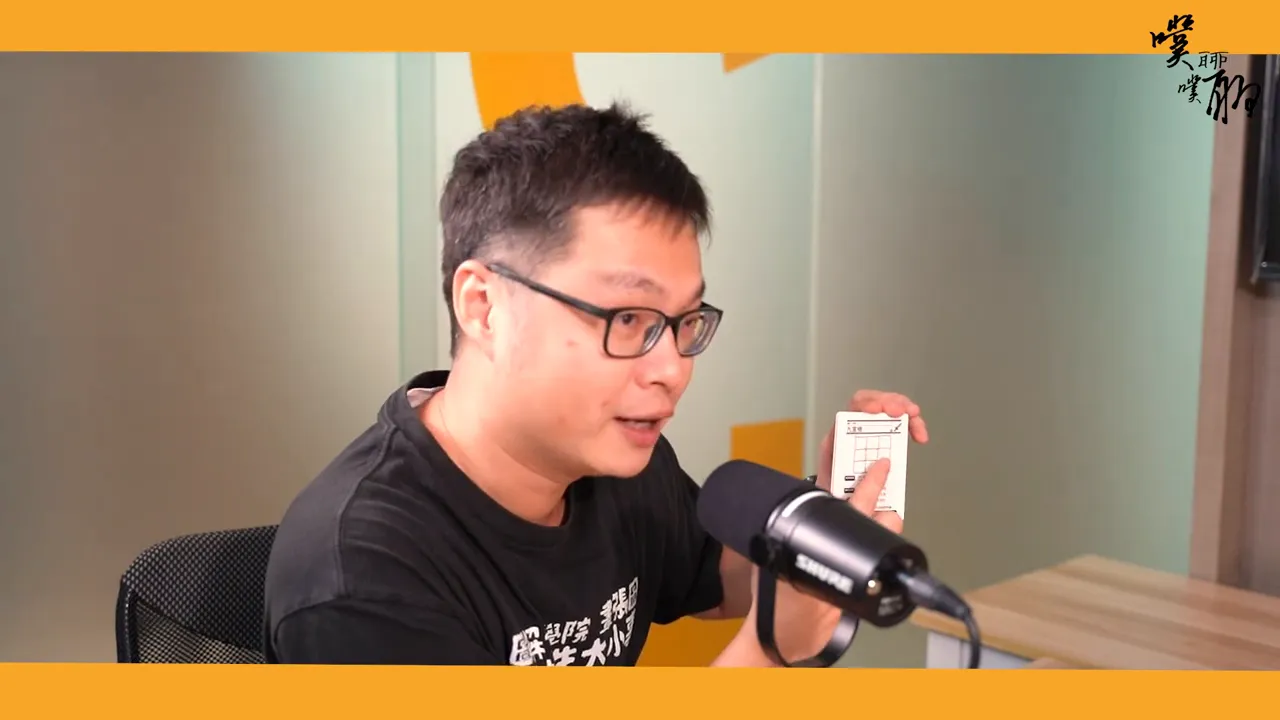 講者在麥克風前手持卡牌,卡片上清楚可見九宮格圖示,並以手指指向卡面