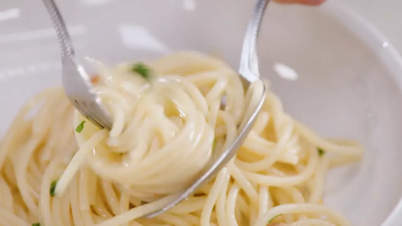 close-up of two forks twirling spaghetti showing a glossy emulsified sauce and parsley