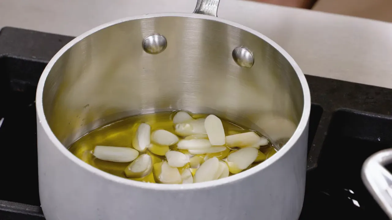 sliced garlic cloves sitting in olive oil in a saucepan