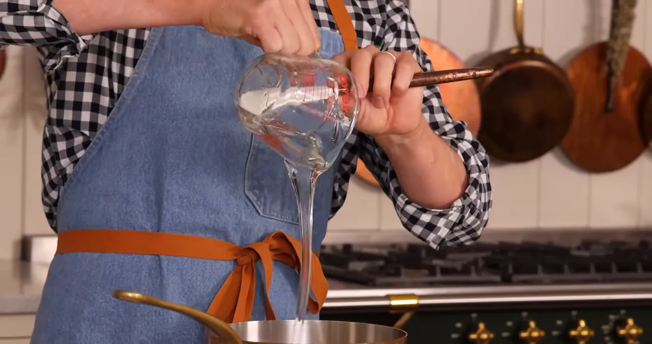 Pouring clear corn syrup from a measuring cup into a saucepan over the stove