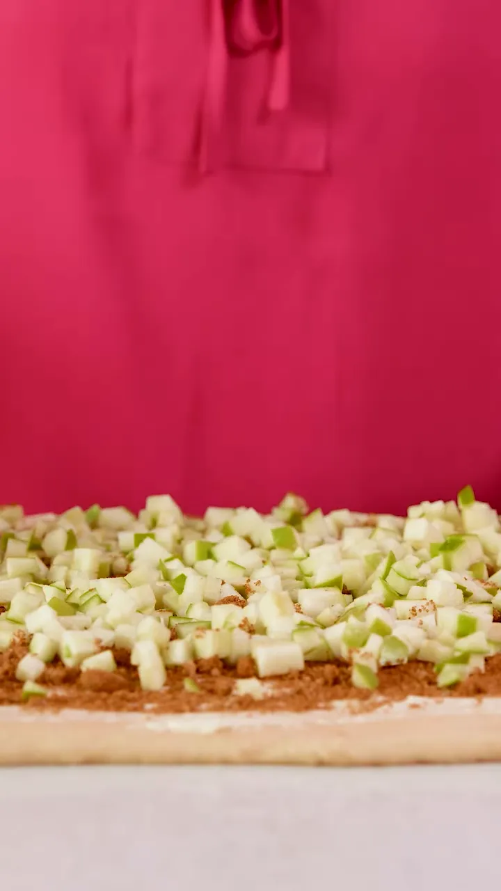 diced green apples evenly scattered over a cinnamon-sugar layer on rolled dough, ready for caramel