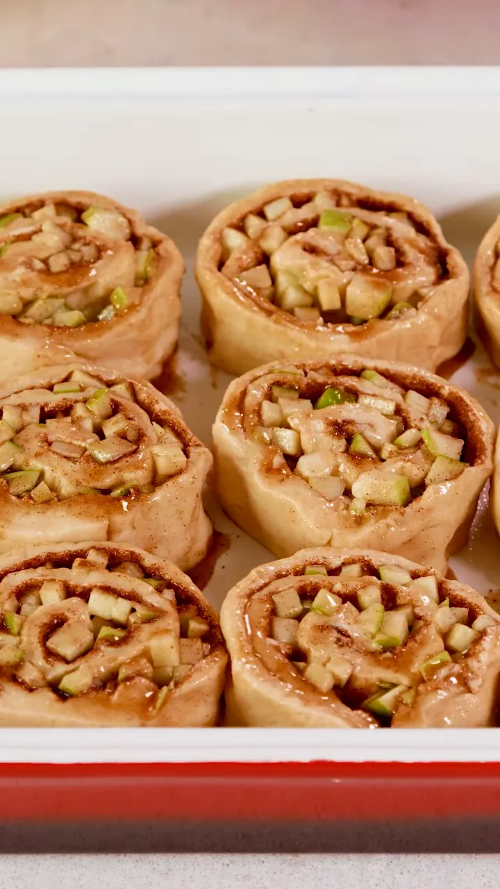 uncooked apple cinnamon rolls with diced apples and cinnamon filling arranged in a red baking pan